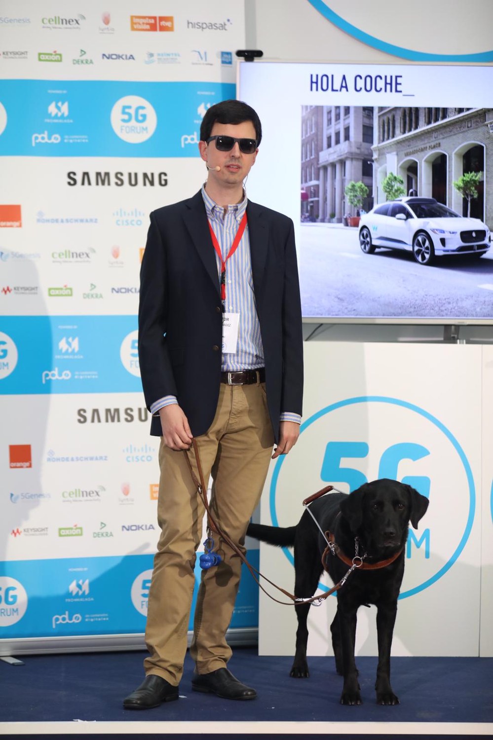 Aitor Fernández interviene en el 5G Forum 2019 junto a su perro guía, ante una pantalla sobre movilidad autónoma.