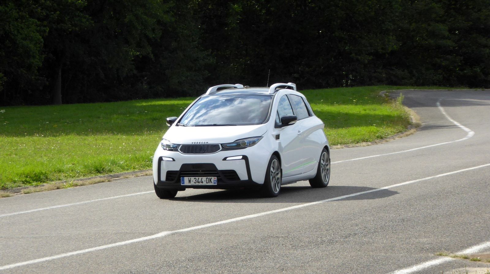 Coche eléctrico blanco con sensores en el techo, en una curva de la pista de pruebas