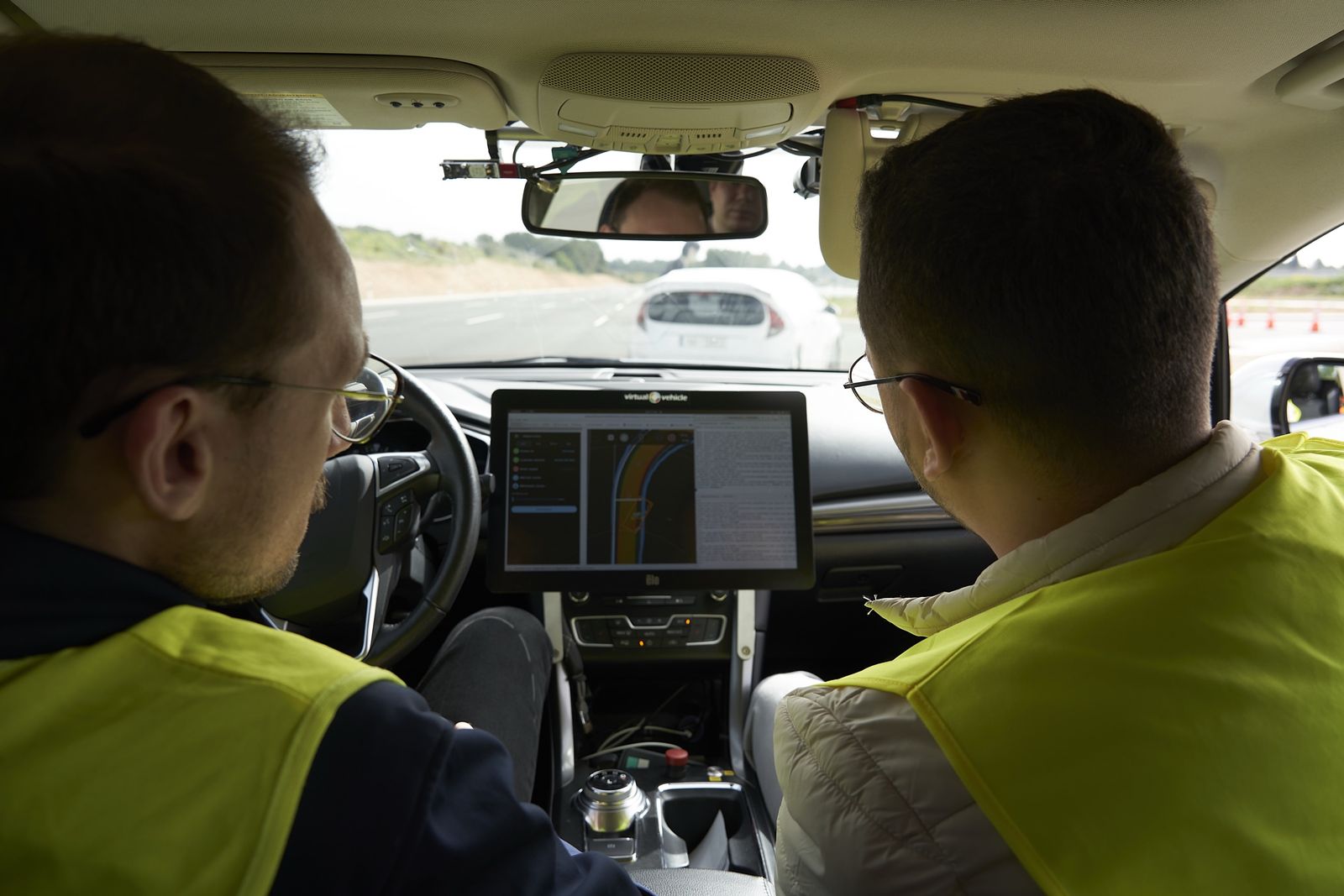 Dos técnicos con chaleco en un coche de pruebas, con una pantalla de datos en el salpicadero